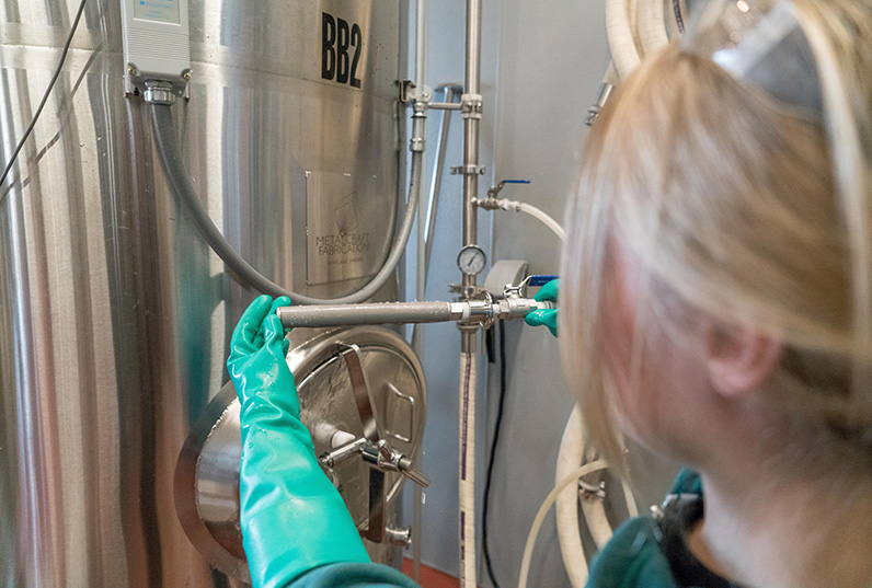 A woman is employed by a global manufacturing firm working on a beer keg in a brewery.